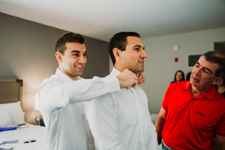 groom getting help from his brother to tie his tie while dad looks over to check the progress.