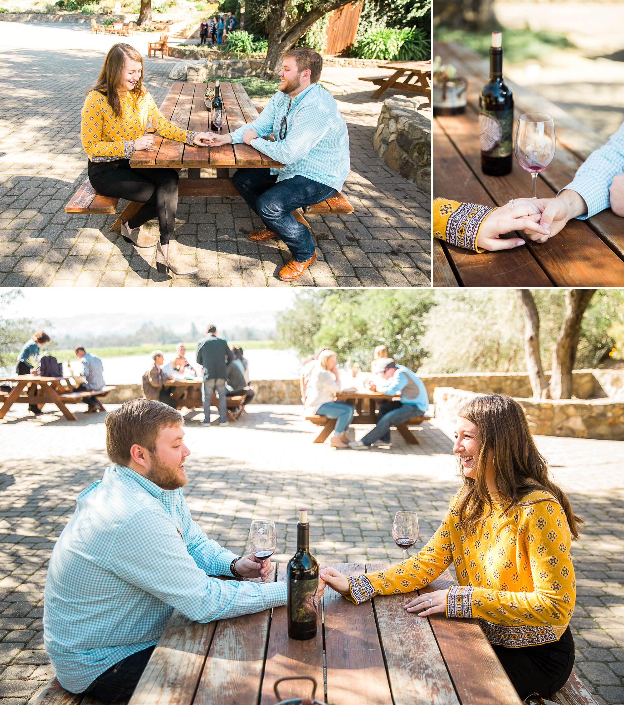 man and woman seated at a picnic table holding hands with a bottle of wine